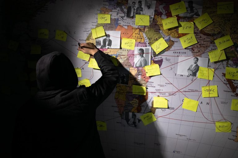 back-view-man-planning-hacker-attack-dark-room-man-writing-wall-with-stickers-photographs-red-threads-planning-conspiracy-hacking-concept