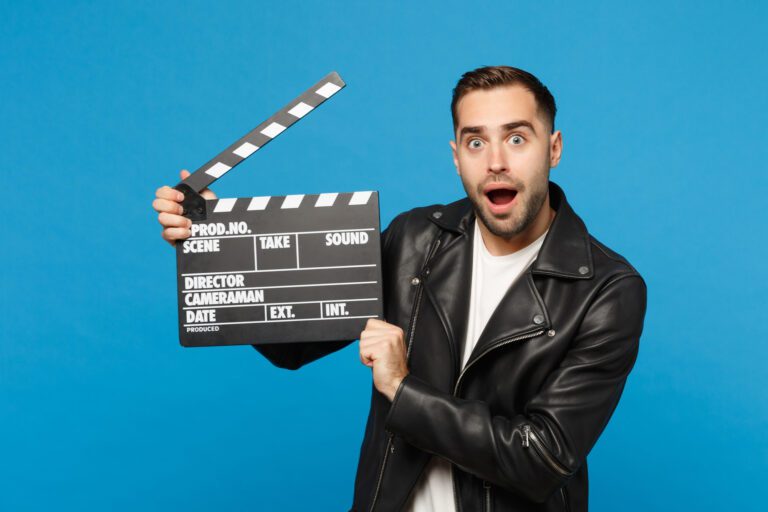 handsome-stylish-young-unshaven-man-black-jacket-white-t-shirt-hold-hand-film-making-clapperboard-isolated-blue-wall-background-studio-portrait-people-lifestyle-concept-mock-up-copy-space