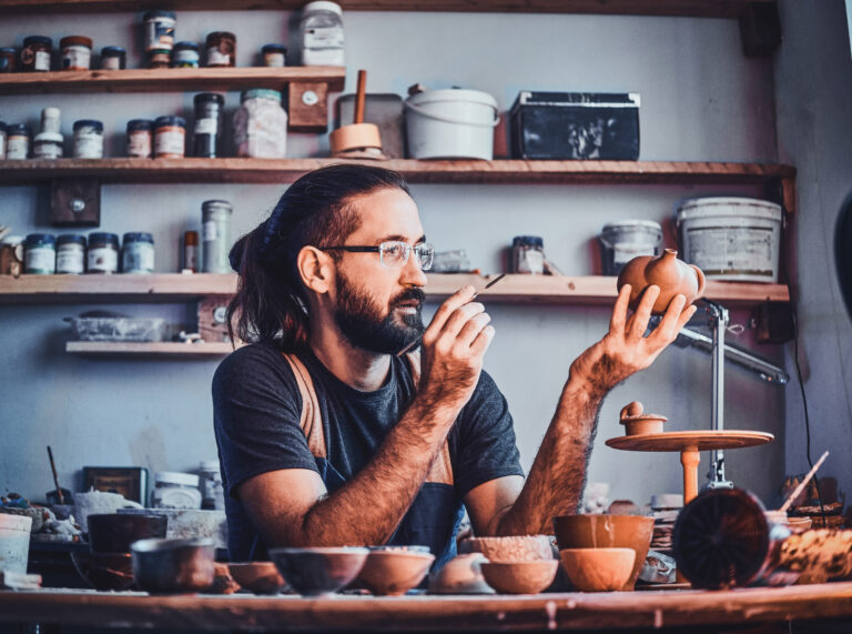 Hardworking man is looking at his own work, ceramic teapot